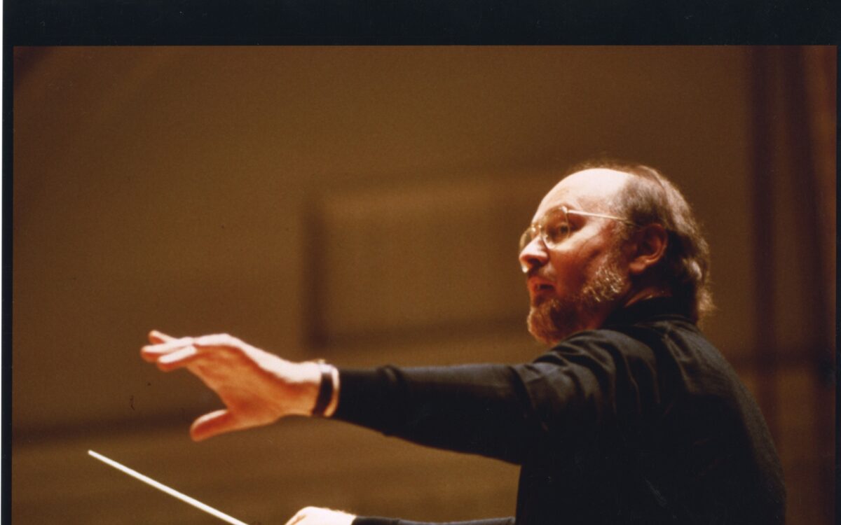 John Williams holds a baton while wearing a black turtleneck and a wristwatch